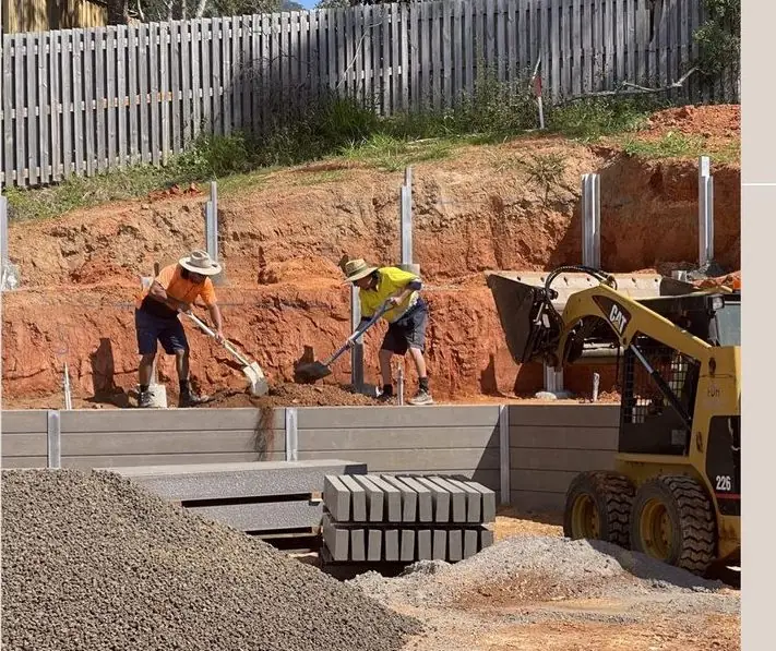 Crew placing drainage gravel behind a sleeper wall