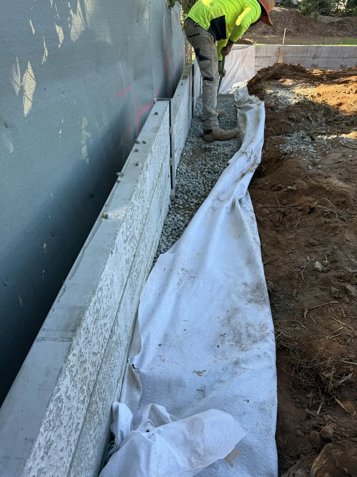 Geofabric and drainage gravel installed behind a concrete sleeper retaining wall