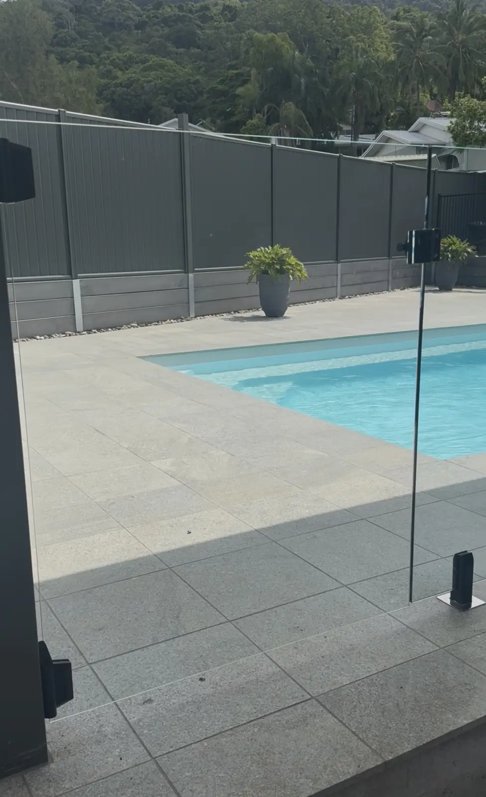 Frameless glass pool gate with black hinges and latch